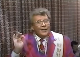 Rod is wearing a violet/red/purple-striped jacket, red tie, white sash with gold butterflies, necklace & white shirt