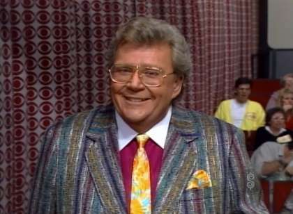 Rod is wearing a multi-colored striped tweed jacket, mottled necktie w/matching pocket square and a maroon shirt with a white collar