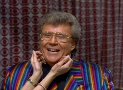 Rod is wearing a rainbow-striped jacket, matching necktie & black shirt