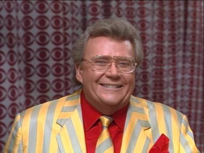 Rod is wearing a yellow and grey striped jacket with matching necktie and a red shirt with matching pocket square
