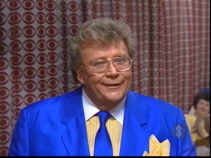 Rod is wearing a blue jacket with matching necktie and yellow shirt with white pinstripes, a white collar and matching pocket square