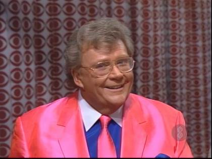 Rod is wearing a pink silk jacket, matching necktie, a dark-blue shirt with white collar & matching pocket square