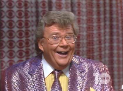 Rod is wearing a shiny purple jacket, matching necktie, yellow shirt with white pinstripes & white collar with matching pocket square