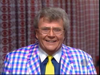Rod is wearing a blue & pink gingham jacket, yellow necktie, dark-blue shirt with a white collar & matching pocket square
