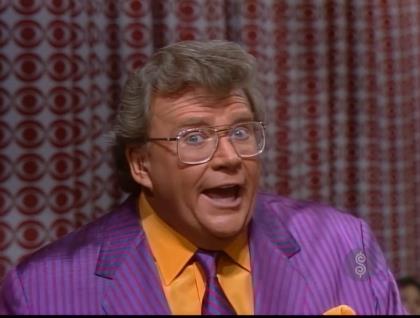 Rod is wearing a purple/grey striped jacket, matching necktie & an orange shirt