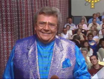 Rod is wearing a shiny purple vest & blue-green-striped collarless silk shirt w/matching pocket square