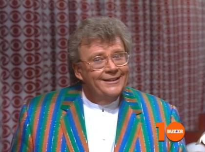 Rod is wearing a green/blue/orange-striped jacket and white collarless shirt