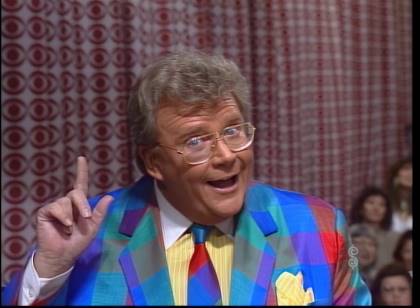 Rod is wearing a multi-colored gingham jacket & matching neck tie and a yellow pin-striped shirt with white collar and matching pocket square