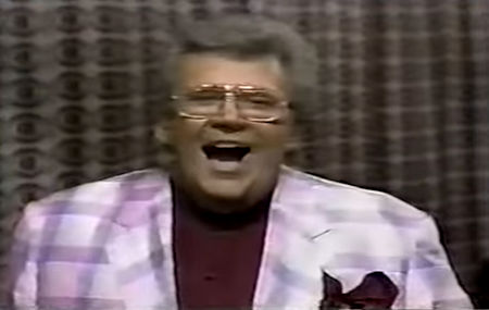 Rod is wearing a pink-gingham jacket & maroon collarless shirt with matching pocket square