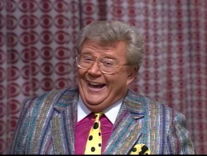 Rod is wearing a multi-colored striped tweed jacket, maroon shirt with white collar, yellow with black polks-dotted necktie and matching pocket square