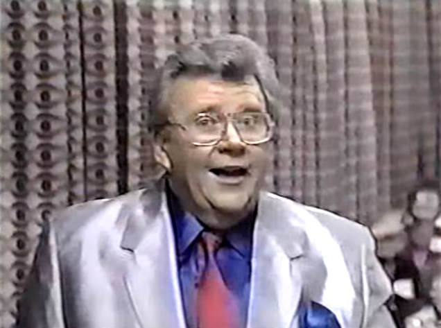 Rod is wearing a shiny grey jacket, red necktie & blue silk shirt with matching pocket square