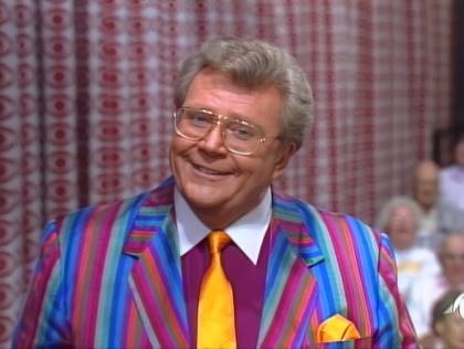 Rod is wearing a multi-colored striped jacket, maroon shirt with white collar & a gold necktie with matching pocketsquare