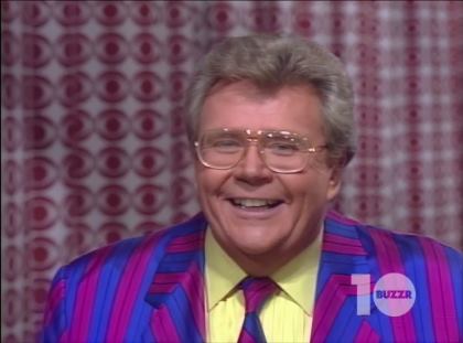 Rod is wearing a blue and purple striped jacket with matching necktie and a light-yellow tuxedo shirt