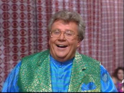 Rod is wearing a shiny green vest & blue/green striped collarless silk shirt with matching pocket square