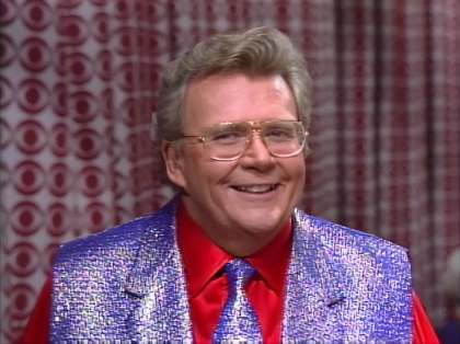 Rod is wearing a shiny purple vest, matching necktie & red silk shirt