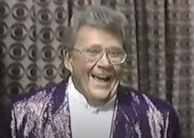 Rod is wearing a shiny purple jacket & white collarless silk shirt