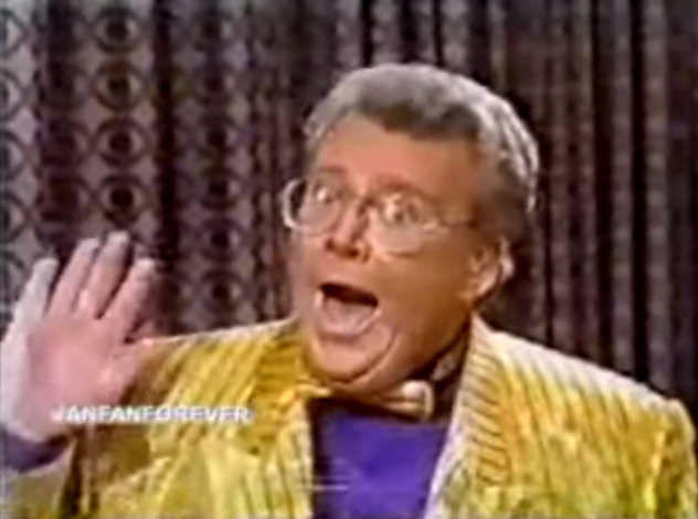 Rod is wearing a shiny yellow/black pin-striped jacket, matching bow-tie & purple collarless silk shirt
