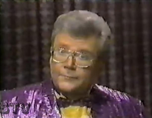 Rod is wearing a shiny purple-striped jacket, matching bow tie & yellow silk shirt