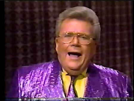 Rod is wearing a shiny purple/purple-striped jacket, matching necktie & yellow shirt