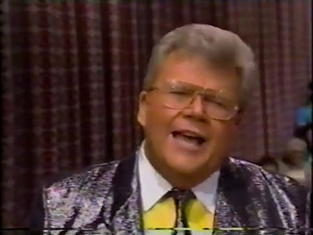 Rod is wearing shiny black jacket with matching necktie & yellow shirt with white collar