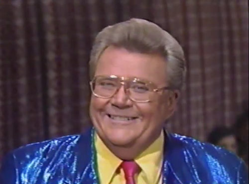Rod is wearing a shiny blue jacket, fuchsia necktie & yellow shirt