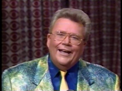 Rod is wearing a shiny green-yellow-blue mottled jacket, dark-blue silk shirt and yellow necktie with matching pocket square