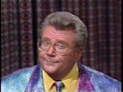 Rod is wearing a shiny blue/purple jacket, matching necktie and yellow shirt