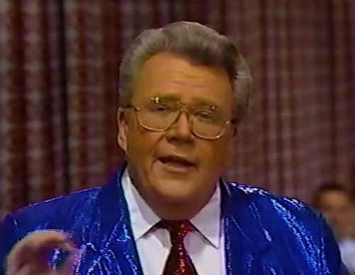 Rod is wearing a shiny blue jacket, shiny red neck tie & white shirt