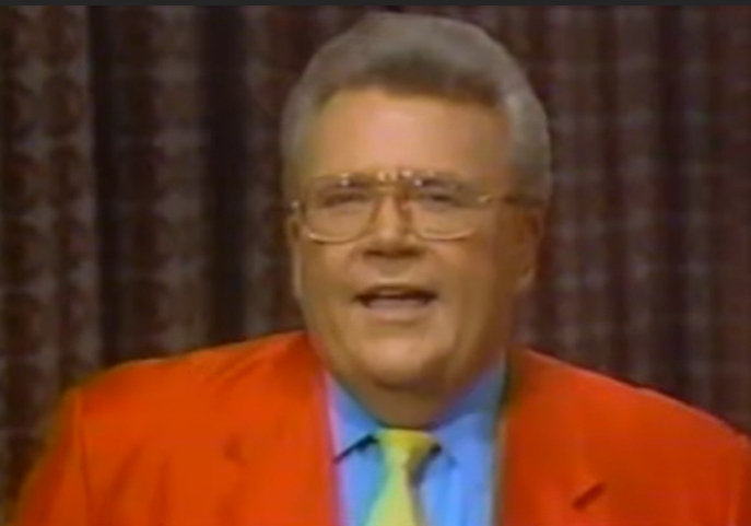 Rod is wearing a red-orange jacket, powder-blue shirt & yellow necktie