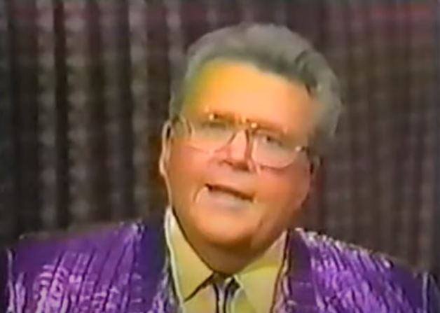 Rod is wearing a shiny purple/purple-striped jacket with matching necktie & yellow shirt