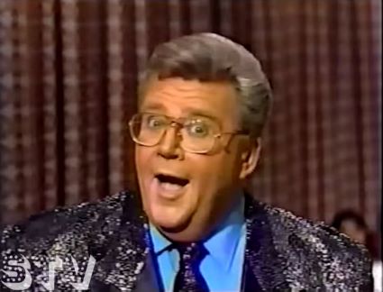 Rod is wearing a Rod is wearing a black sequined jacket with matching necktie & light-blue shirt