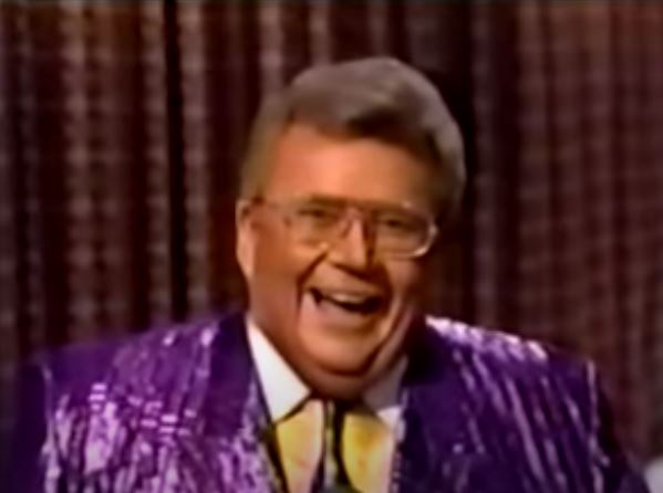 Rod is wearing a shiny purple jacket, matching tie and yellow shirt with a white collar