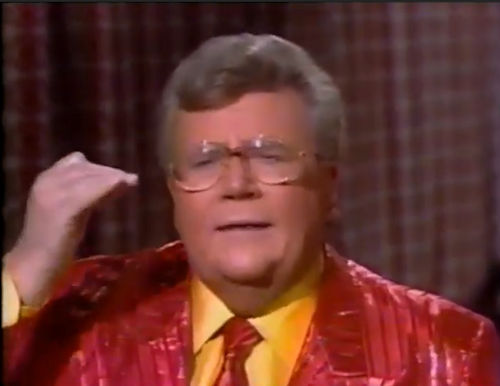 Rod is wearing a shiny red/red-striped jacket, matching necktie & yellow shirt