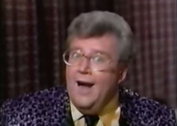 Rod is wearing a purple leopard print jacket, black tie & yellow silk shirt