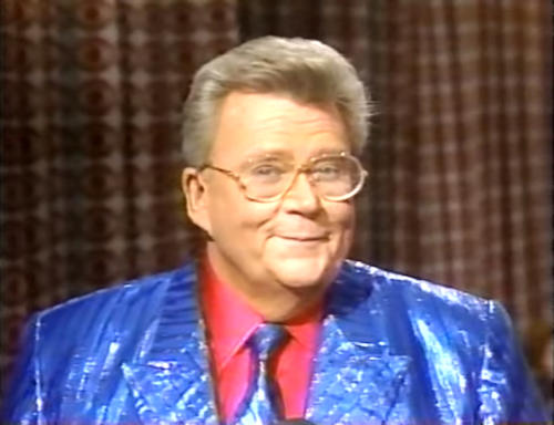 Rod is wearing a shiny blue/blue-striped jacket, matching tie & red shirt