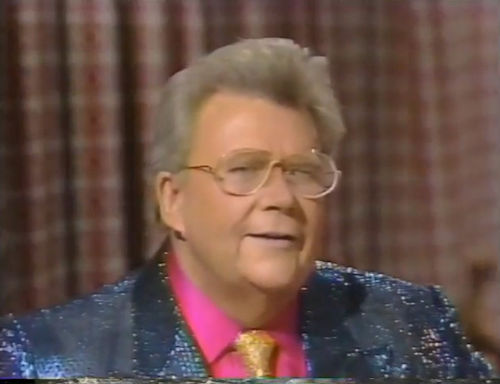 Rod is wearing a purple-blue sequined jacket, gold sequin necktie & pink shirt