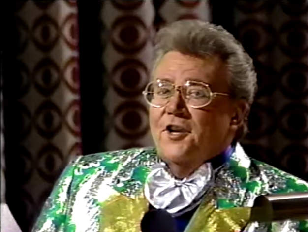 Rod is wearing a shiny green jacket with silver oak-leaves & gold lapels, a silver-frilly bowtie & purple collarless silk shirt