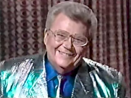 Rod is wearing a shiny seafoam-green jacket, matching necktie and blue silk shirt