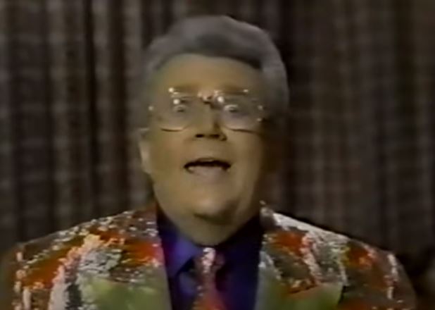Rod is wearing a red & gold sequined jacket with gold lapels and matching tie & dark-purple shirt