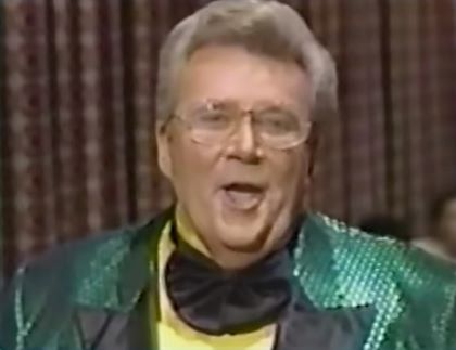 Rod is wearing a shiny green jacket with black lapels, a yellow collarless silk shirt & frilly black bowtie