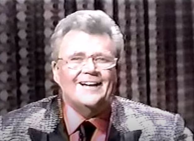 Rod is wearing a silver sequin jacket with black lapels, black neck-tie  & peach silk shirt