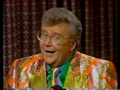 Rod is wearing a shiny orange jacket with gold lapels, shiny green necktie & green shirt