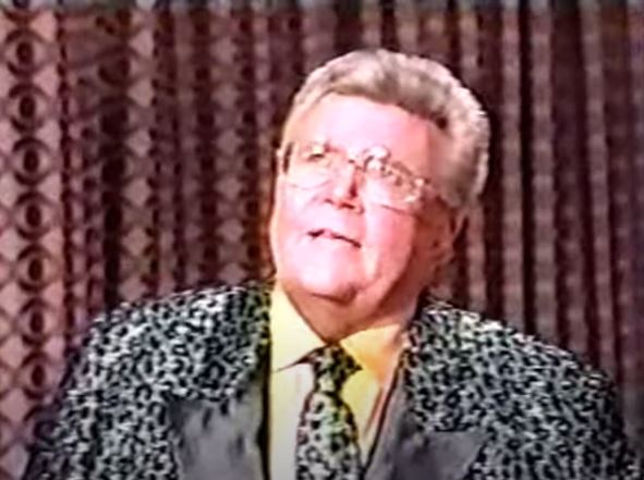 Rod is wearing a shiny silver leopard-print jacket with black lapels, matching tie & yellow shirt