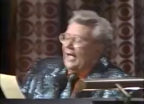 Rod is wearing a dark-green sequined jacket, matching necktie & an orange silk shirt