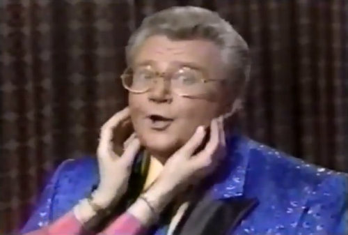 Rod is wearing a blue jacket with shiny blue dots & black lapels, a matching necktie & yellow shirt