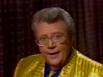 Rod is wearing a shiny yellow/yellow striped jacket, matching necktie & blue collarless silk shirt