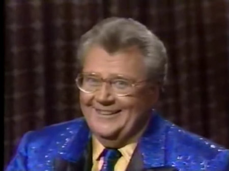 Rod is wearing a blue jacket with shiny spots & black lapels, a matching necktie & yellow shirt