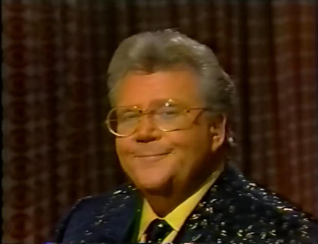 Rod is wearing a black jacket with gold speckles, matching neck tie & yellow shirt