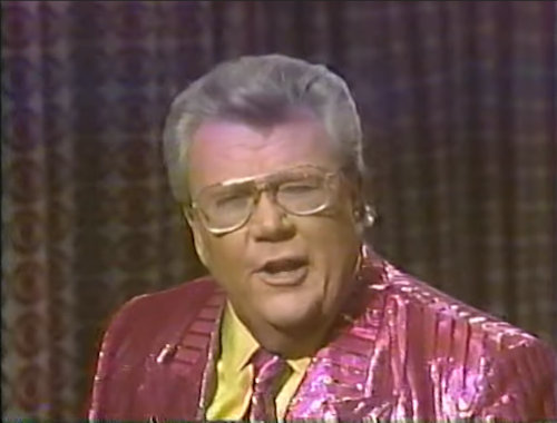 Rod is wearing a shiny pink/pink-striped jacket, matching necktie & yellow silk shirt