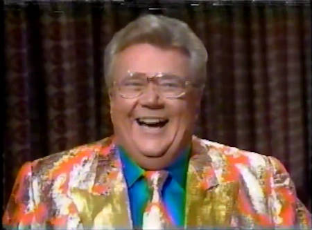 Rod is wearing an orange jacket with silver splotches & gold lapels with a matching tie & blue silk shirt